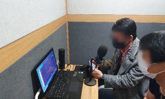 녹음 부스에서 마이크와 노트북으로 스크립트를 발화하는 참여자