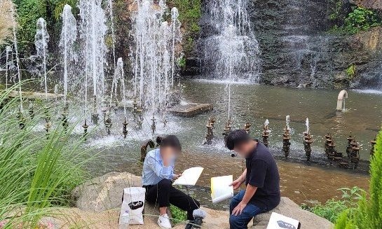 분수대 앞 바위에 앉아 대화를 녹음하는 두 참여자